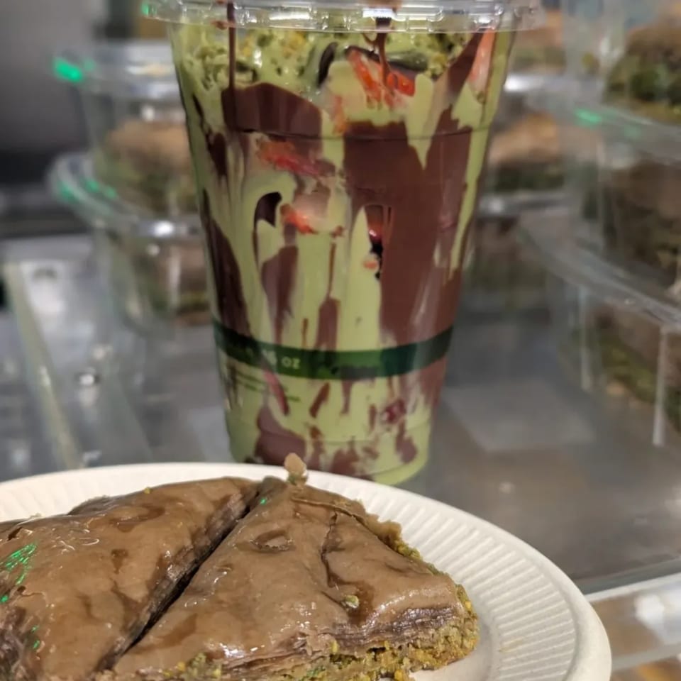 Two pieces of chocolate baklava on a white plate with a green and chocolate drink in the background.