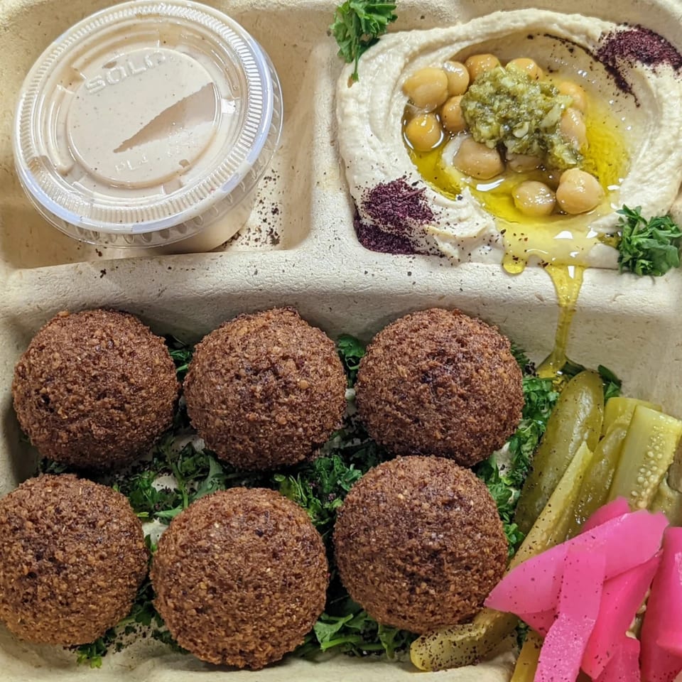 A Mazaj Mediterranean falafel platter with hummus, falafel, pickles, and a side of sauce.